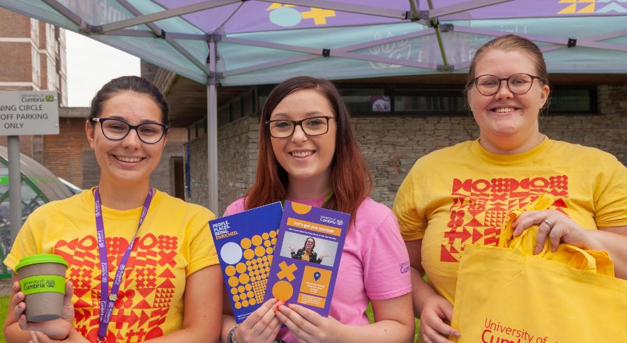 Three Cumbria students stand at a stall smiling