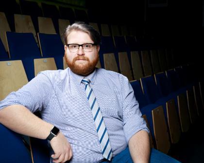 Mitch Bridgewater - Stanwix Theatre Manager, Photograph of a man seated in a theatre looking at the camera. He is wearing a blue shirt and tie with glasses and a beard.