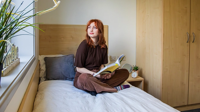Student seating on a bed reading a book