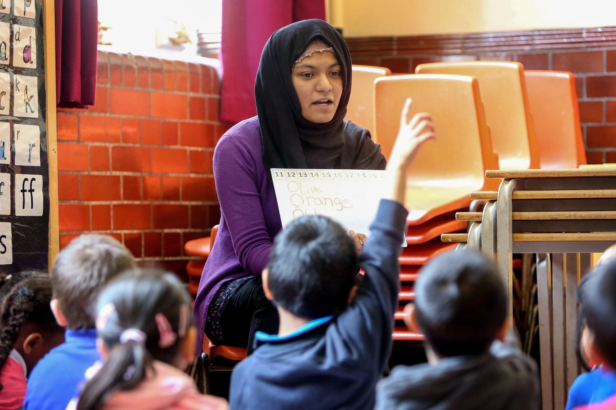A woman sits in front of a primary school class teaching words that begin with O