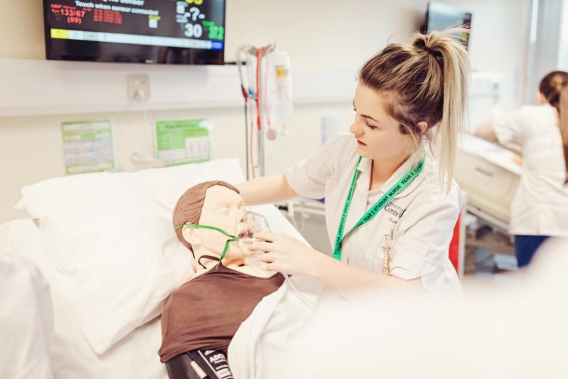 A nursing student putting an oxygen mask on a dummy person